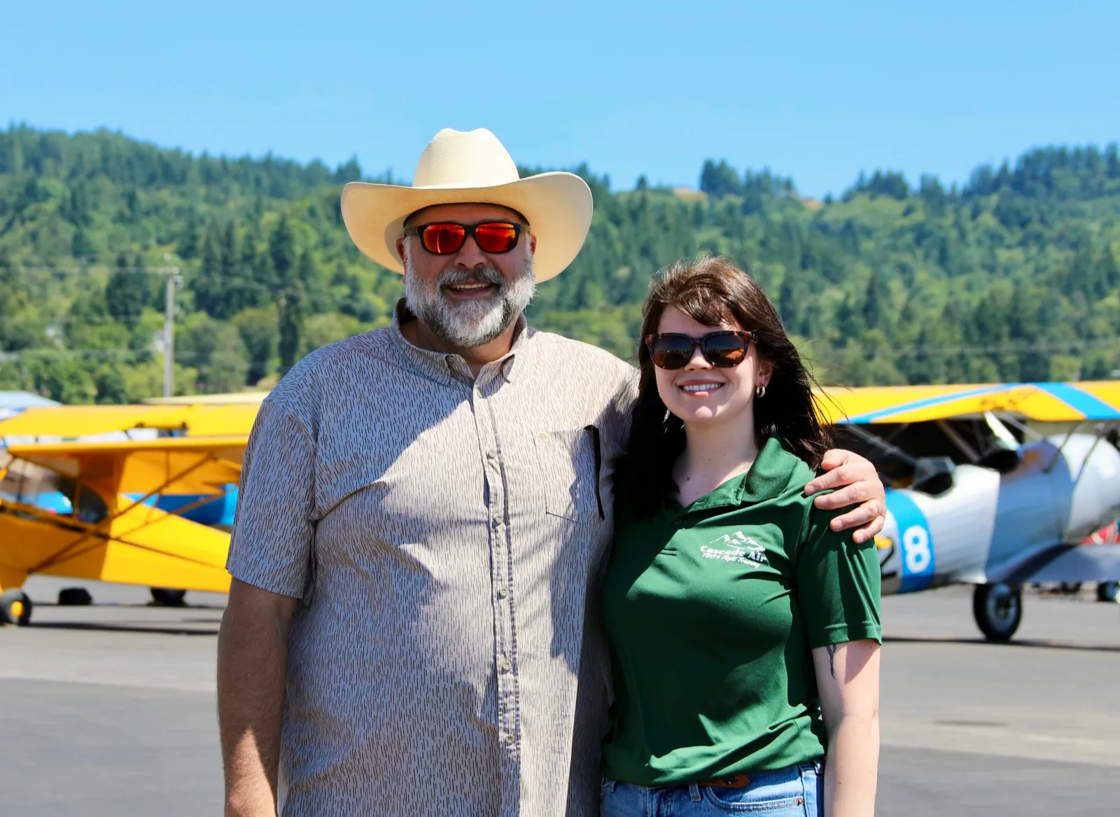 Jessica Statham and her father standing on the KKLS ramp with biplanes in the background.
